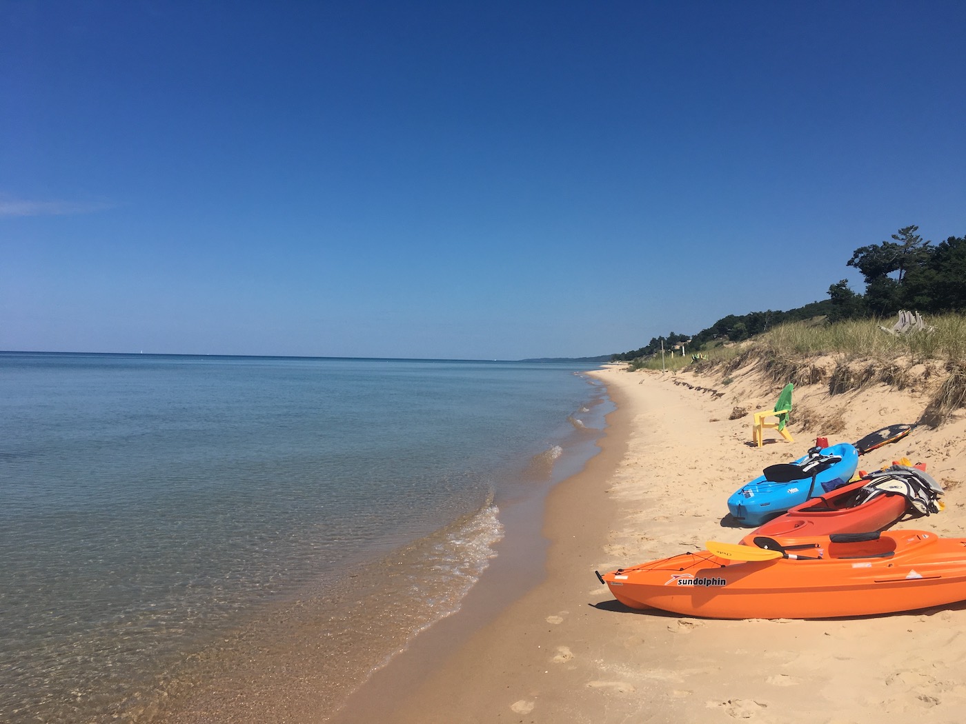 Kayaks rest on the shore of Lake Michigan against a brilliant blue sky